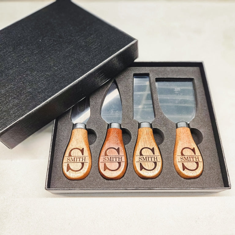 Set of four cheese knives with wooden handles, engraved with personalized monogram names design, in a black gift box.