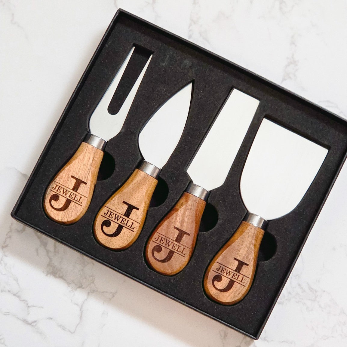 Set of four cheese knives with wooden handles, engraved with personalized monogram names design, in a black gift box.