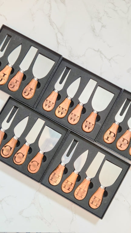 Set of four cheese knives with wooden handles, engraved with personalized monogram names design, in a black gift box.